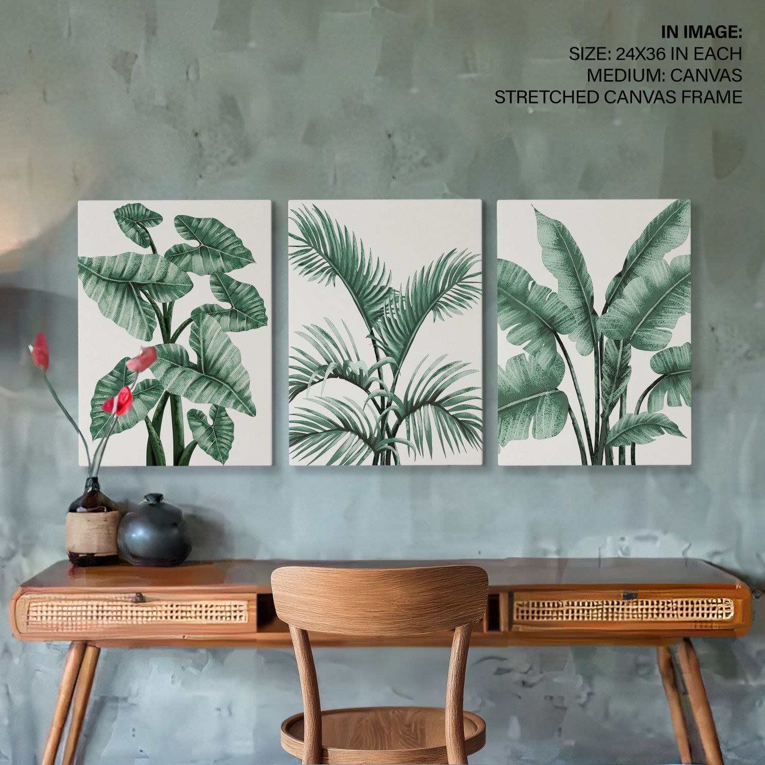 Set of 3 green botanical leaf prints hung above a wooden desk — tropical leaves in soft greens with natural broad canvas frames, lifestyle room mockup